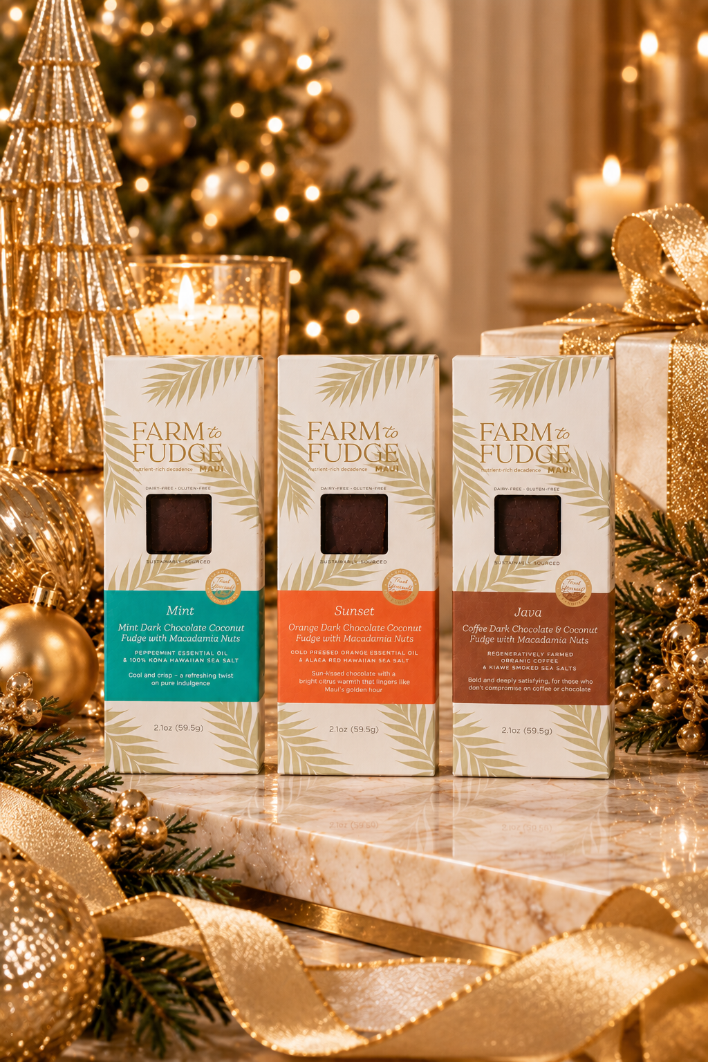 Three boxes of Farm to Fudge chocolate fudge pieces displayed on a marble surface with a festive holiday background featuring gold ornaments, a lit candle, and wrapped gifts. The boxes are labeled Mint, Sunset, and Java.