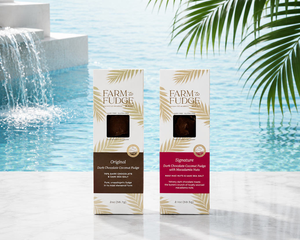 Two boxes of Farm to Fudge dark chocolate coconut fudge in front of a water fountain with greenery.